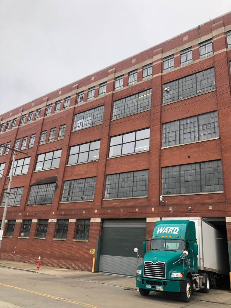 Large brick building with numerous windows and a green delivery truck parked in front.