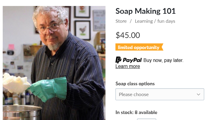 Instructor holding a bowl of soap mixture, wearing teal gloves, in a workshop setting with various supplies in the background.