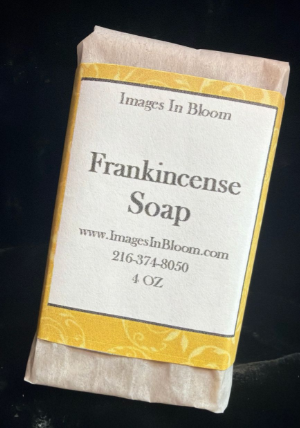 A bar of frankincense soap wrapped in paper with a white label featuring the product name, website, and weight.